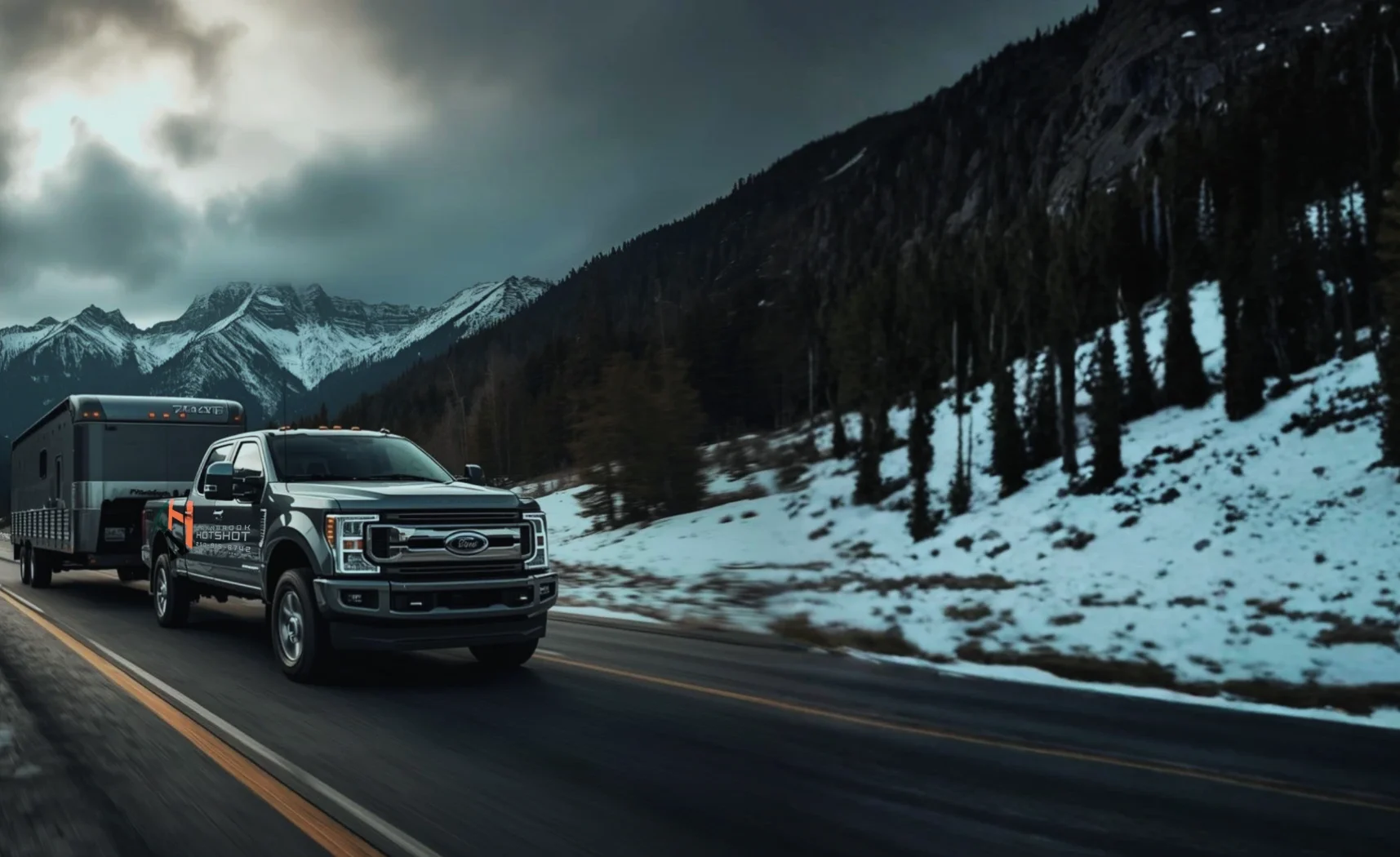 Hotshot truck and flatbed trailer traveling at speed through mountain terrain under overcast skies.
